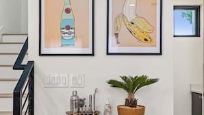 Une cuisine moderne avec un escalier en bois, une machine à café, une plante en pot et deux œuvres d’art encadrées accrochées au mur.