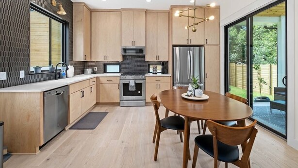 Une cuisine moderne avec des meubles en bois, des appareils électroménagers en acier inoxydable et un coin repas comprenant une table ronde et des chaises.