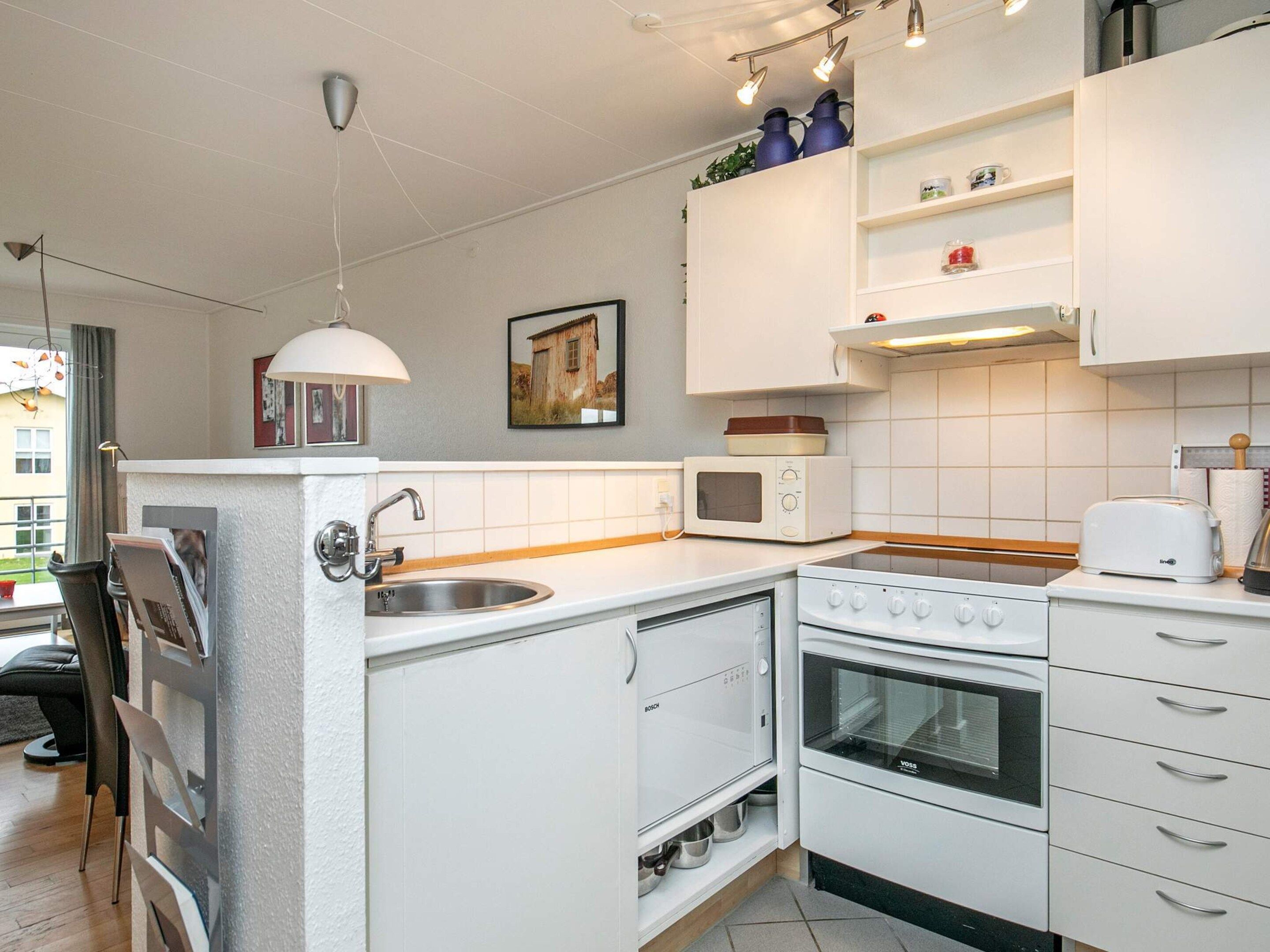A compact kitchen with white appliances, a built-in oven, a microwave, and a sink.