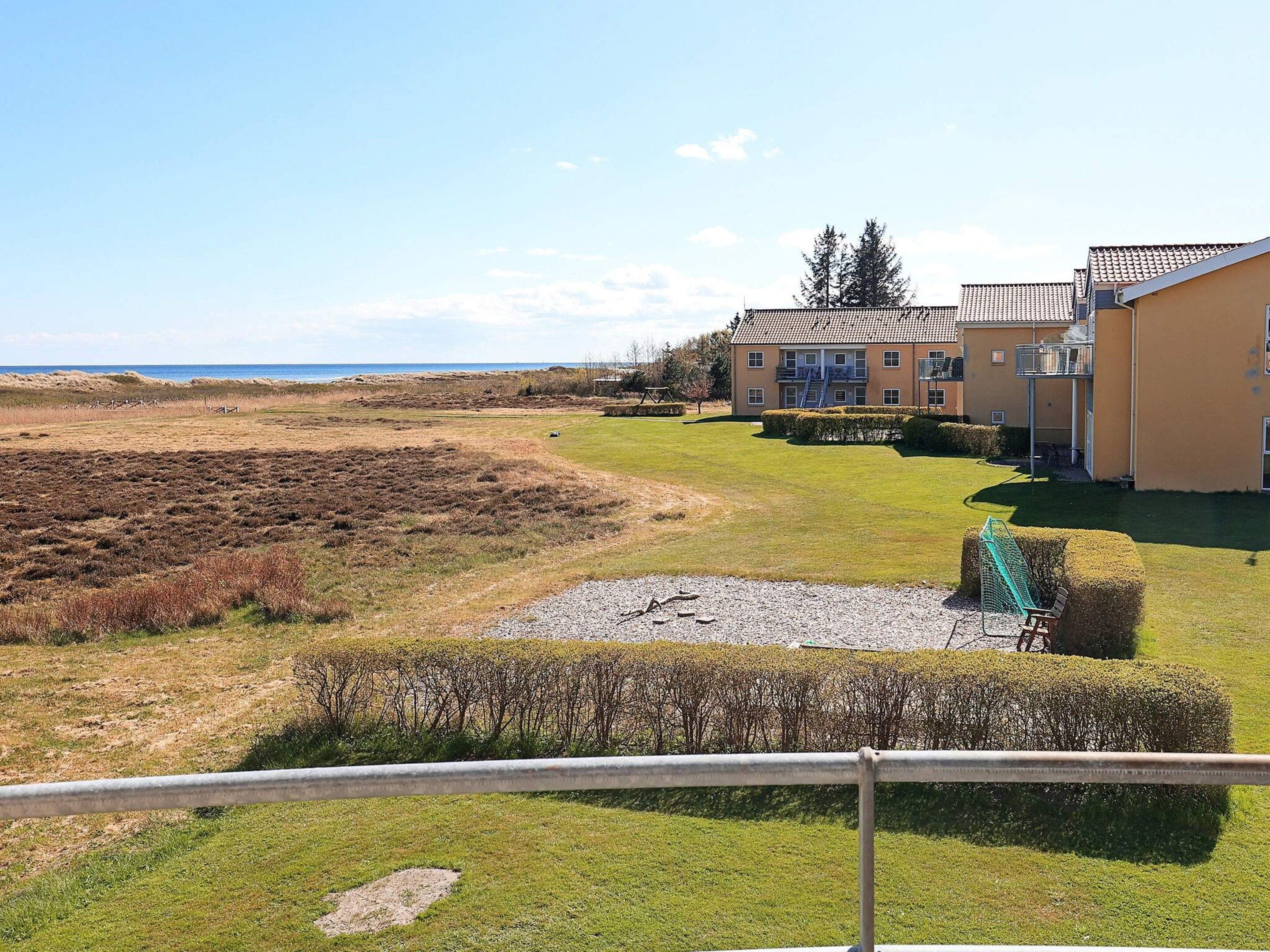 A residential area with a grassy field, a small pond, and a building with a balcony.