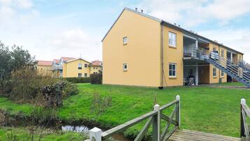 A yellow building with a staircase leading to a balcony, a wooden deck, and a small stream in the foreground.