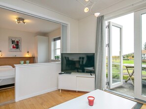 A modern hotel room with a flat-screen TV, a white table, and a sliding glass door leading to an outdoor area. - 4 Person Holiday Home in Hals (Hals)