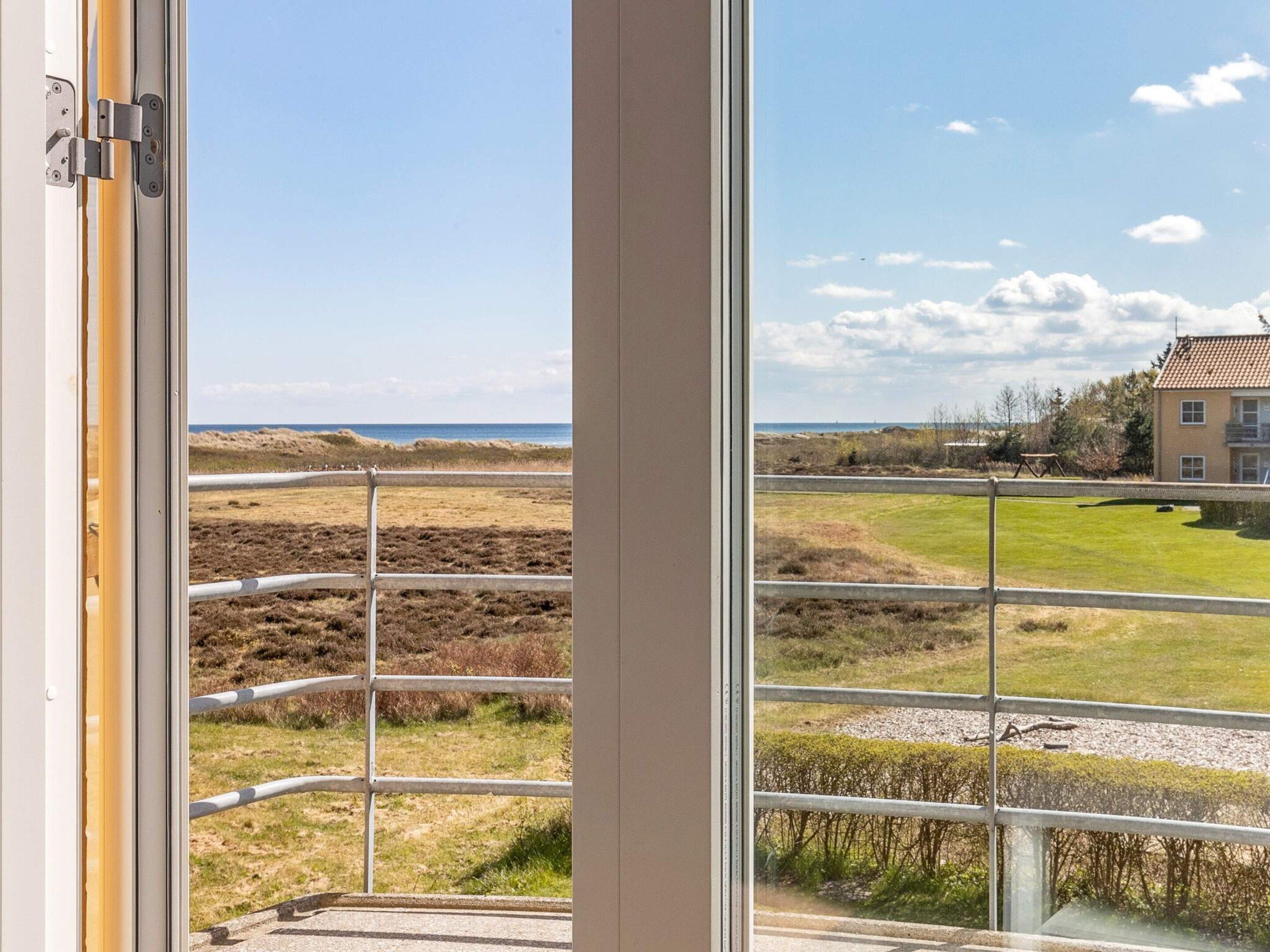 A view from a window with a metal railing, overlooking a grassy area with a building in the distance.