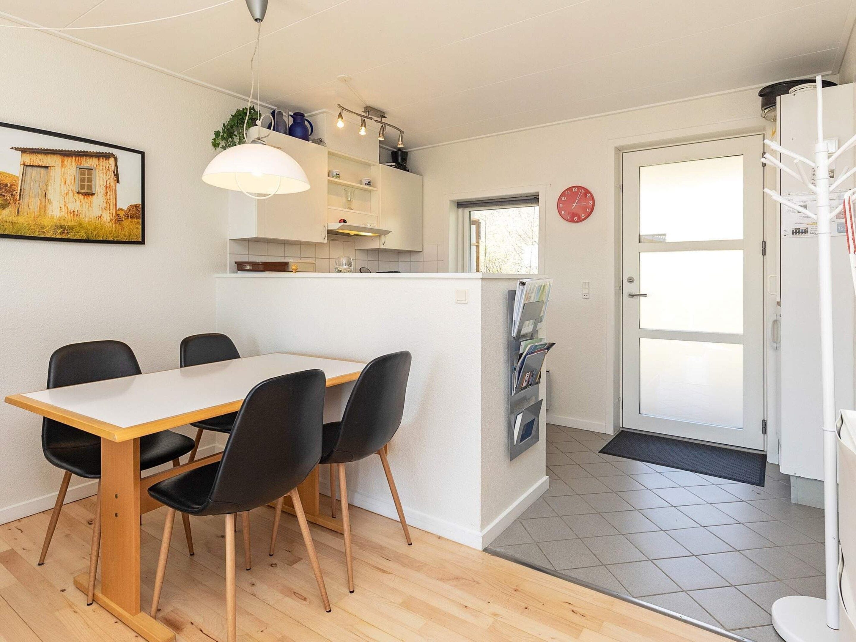 A modern kitchen with a dining area, featuring a white table, black chairs, and a pendant light.