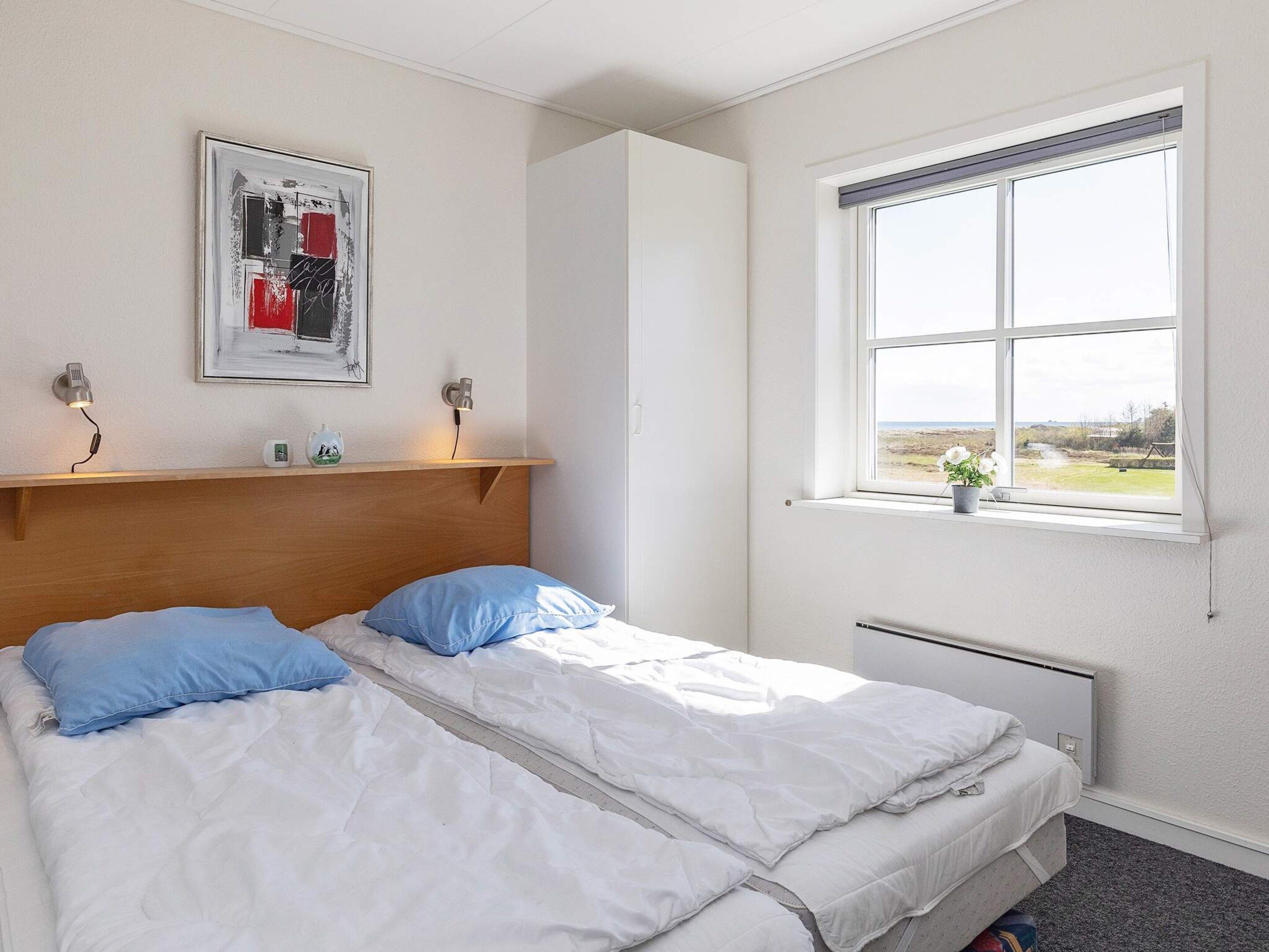 A bedroom with a bed, a headboard, a window with a view, and a wall-mounted artwork.