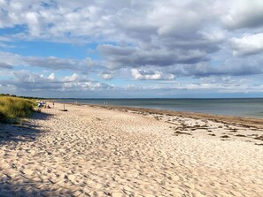 A sandy beach with people and tents, a grassy dune area, and a calm sea under a cloudy sky.