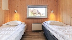 Une chambre avec deux lits, des murs en bois, une fenêtre avec des stores et un radiateur fixé au mur.
