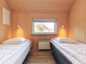 A room with two beds, wooden walls, a window with blinds, and a wall-mounted heater. - 4 Star Holiday Home in Vaeggerlose (Vaeggerlose)