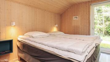 A wooden-paneled room with a bed, two wall-mounted lights, and a window with a view of greenery.