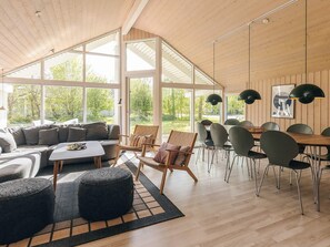 A spacious living area with a large window, a dining table, and modern furniture. - 4 Star Holiday Home in Vaeggerlose (Vaeggerlose)