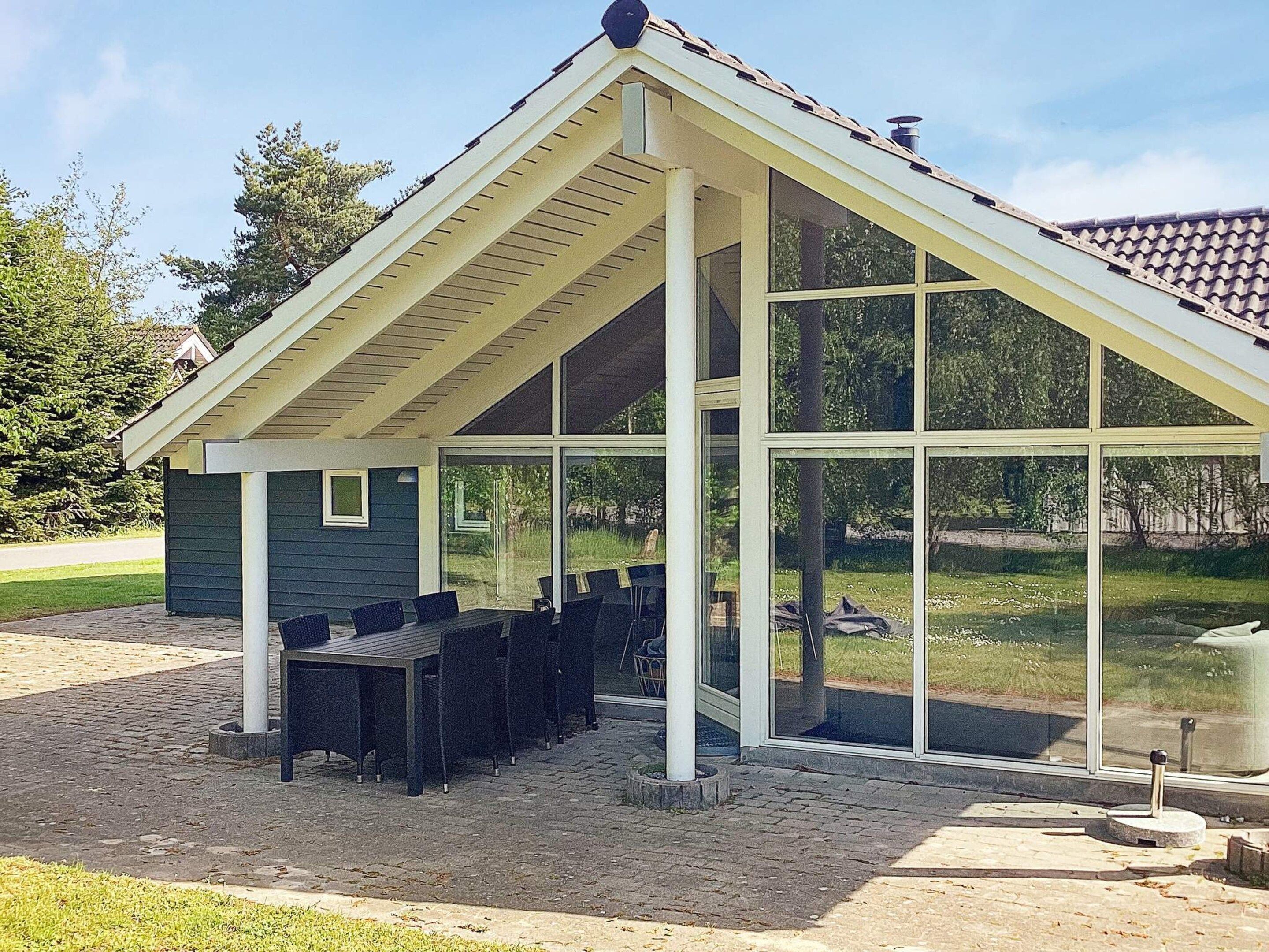 A covered outdoor seating area with a table and chairs, large windows, and a sloped roof.
