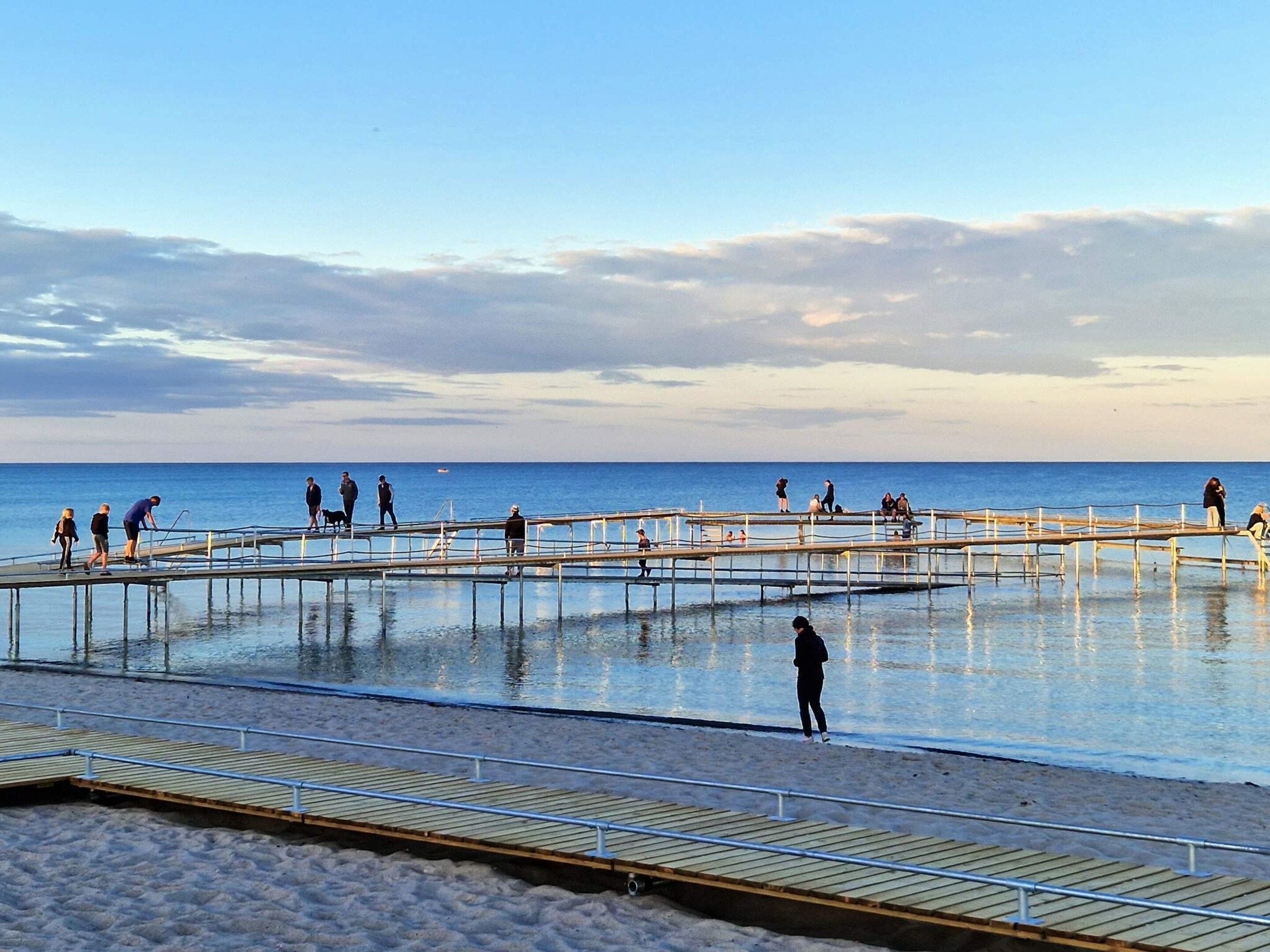 A pier extending into calm waters with people walking and standing on it.