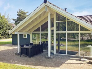 A covered outdoor seating area with a table and chairs, large windows, and a sloped roof. - 4 Star Holiday Home in Vaeggerlose (Vaeggerlose)