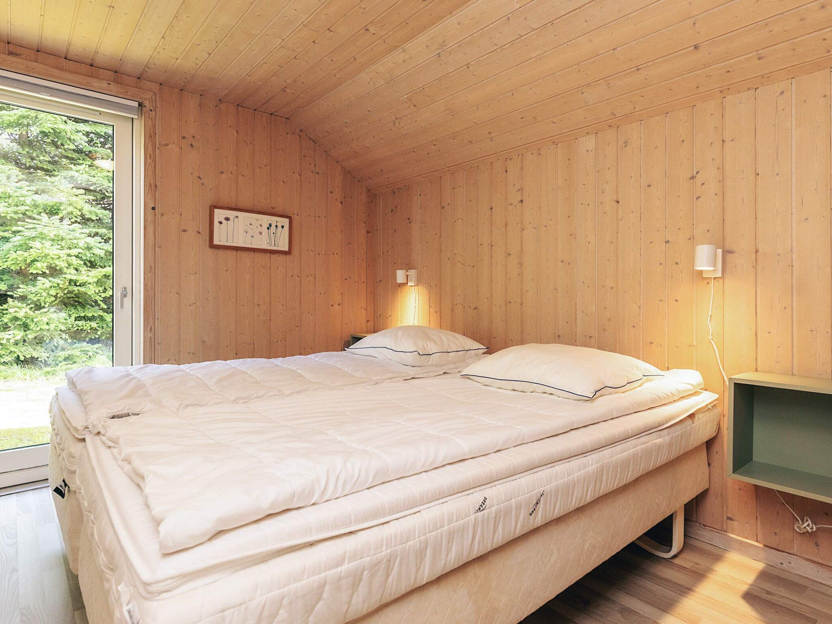 Een slaapkamer met houten lambrisering, een bed, bedlampen en een raam.