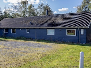 A single-story building with a dark blue exterior, a tiled roof, and a gravel driveway. - 4 Star Holiday Home in Vaeggerlose (Vaeggerlose)