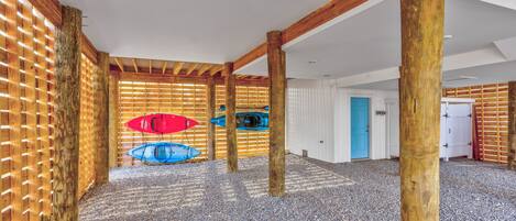 Un espacio al aire libre cubierto con vigas de madera y suelo de grava, con dos kayaks y una sombrilla roja.