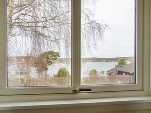A window with a view of a lake, a dock, and a building with a red roof. - 4 Star Holiday Home in Stromstad (Stromstad)