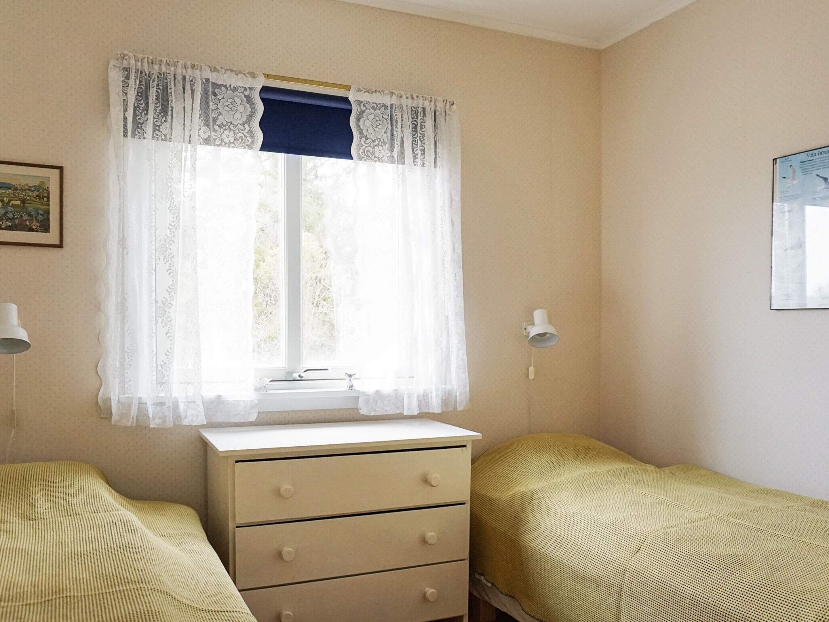 Una habitación con ventana, tocador, dos camas y una lámpara en la pared.