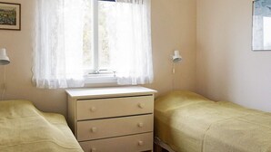 A room with a window, a dresser, two beds, and a wall-mounted lamp.