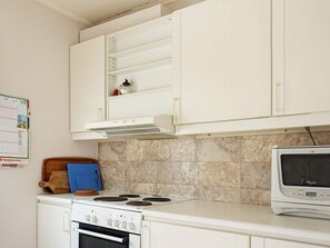 A kitchen with white cabinets, a stove, an oven, a microwave, and a wooden cutting board. - 4 Star Holiday Home in Stromstad (Stromstad)