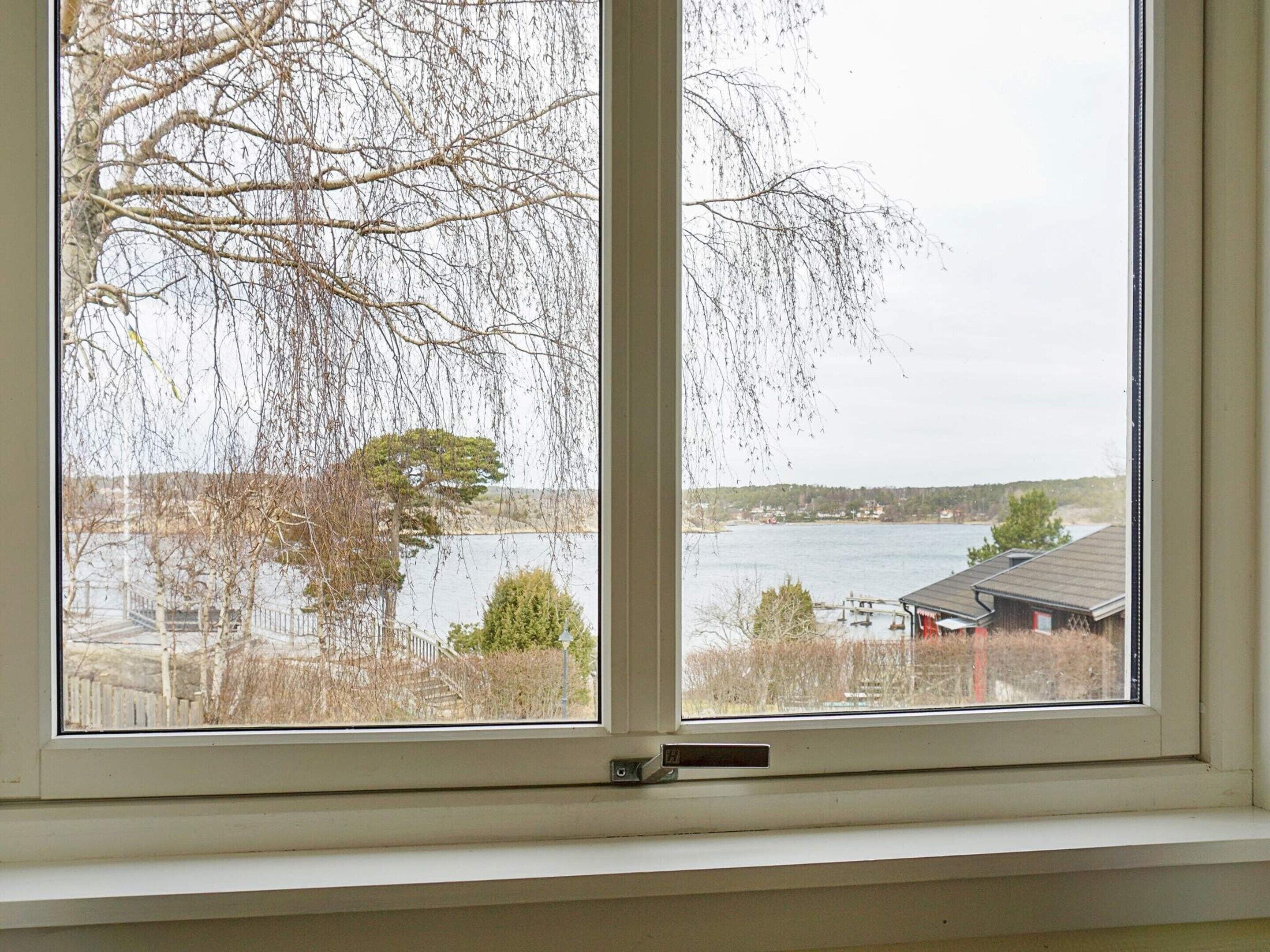 A window with a view of a lake, a dock, and a building with a red roof.
