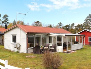 Une maison de plain-pied avec un patio couvert, un petit jardin et, au fond, une grange rouge.