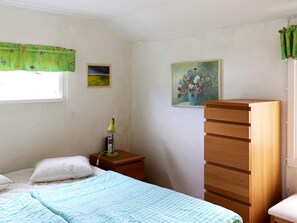 Een slaapkamer met een bed, een nachtkastje, een lamp, een dressoir en twee aan de muur bevestigde schilderijen.