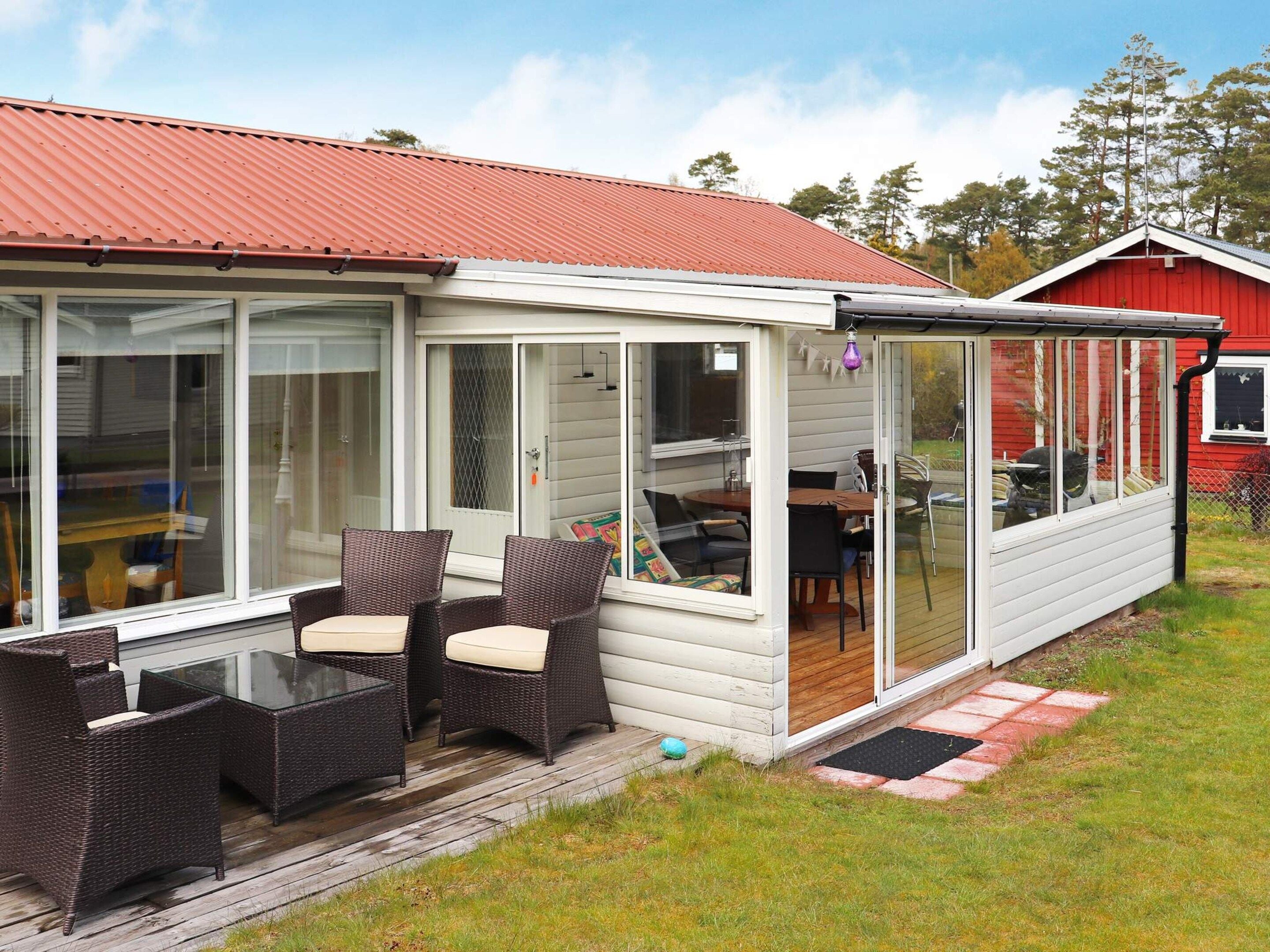 Un espacio al aire libre techado con mobiliario de mimbre y un ventanal que da a una habitación.