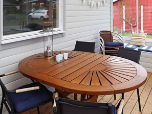 A round wooden table with chairs, a window with a view of a car, and a red building in the background.