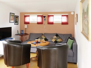 Een woonkamer met een bank, twee fauteuils, een salontafel en een televisie.