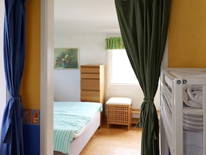 Een slaapkamer met een bed, een houten dressoir, een klein krukje en een ledikant.