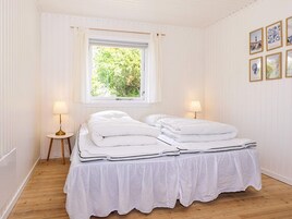 A room with a bed, two bedside lamps, a window with a view of greenery, and framed pictures on the wall.