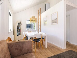 A room with a white dining table, chairs, a bookshelf, a ladder, and framed pictures on the wall.