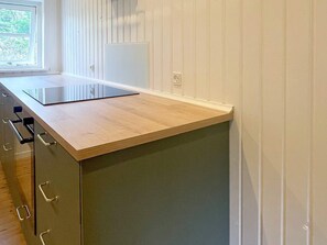 A kitchen with a wooden countertop, a built-in dishwasher, and a window with blinds.