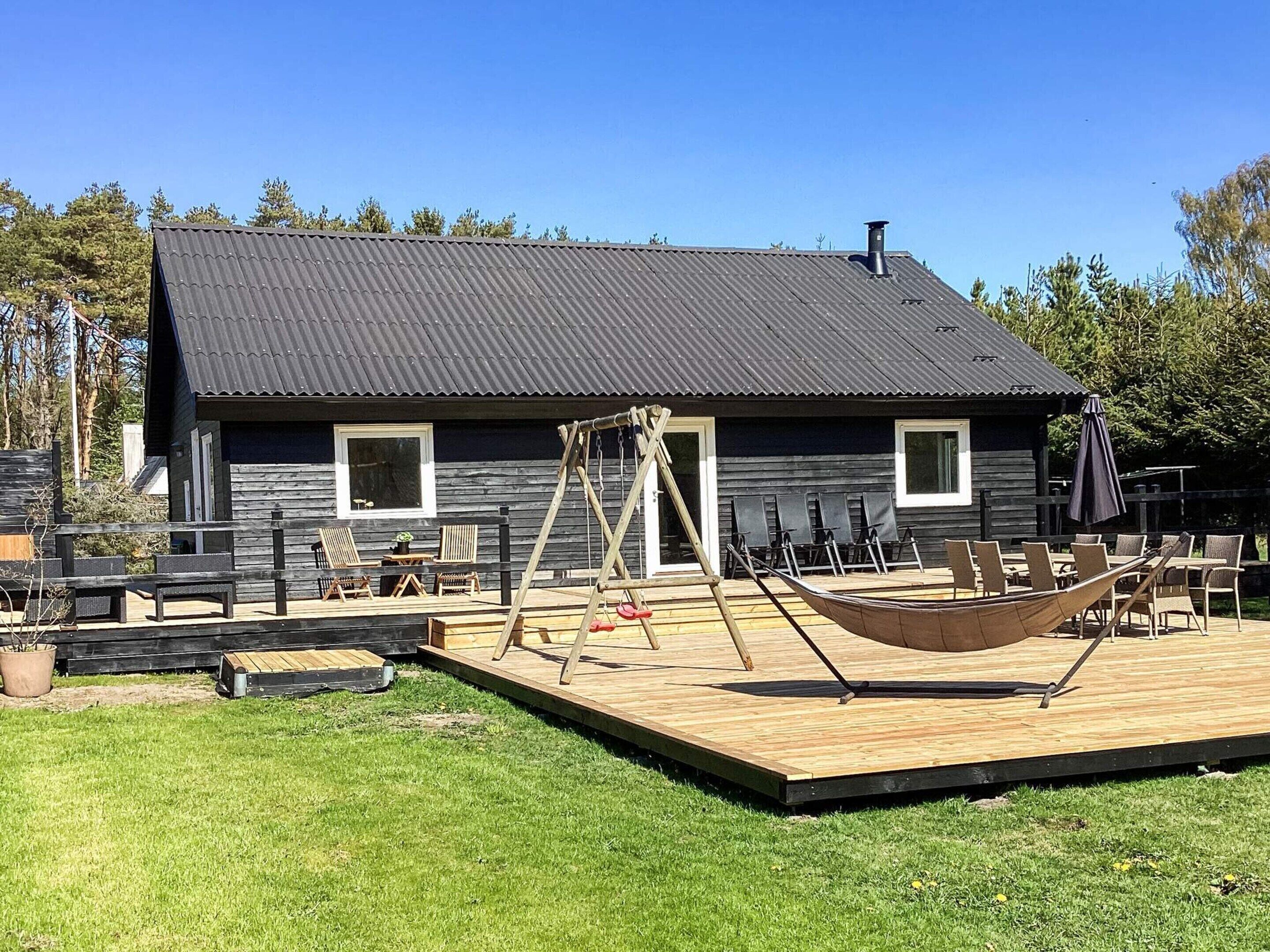 A wooden cabin with a deck, outdoor seating, and a hammock.