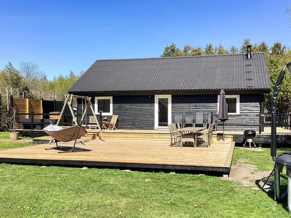 Une terrasse en bois avec des meubles d’extérieur, une balançoire et un barbecue.