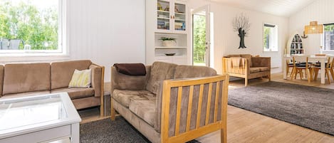 A cozy living room with a sofa, a wooden chair, a glass coffee table, and a bookshelf.