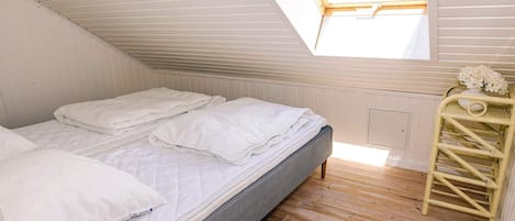 A single bed with white bedding in a room with wooden flooring and a sloped ceiling.
