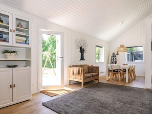 A spacious living area with a sofa, a dining table with chairs, a bookshelf, and a large window.