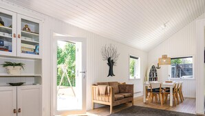 A spacious living area with a sofa, dining table, and chairs, a bookshelf, and a large window. - 4 Star Holiday Home in Hals (Hals)