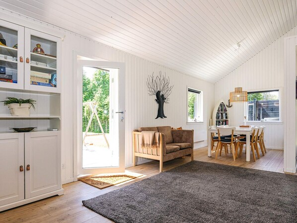 A spacious living area with a sofa, dining table, and chairs, a bookshelf, and a large window.
