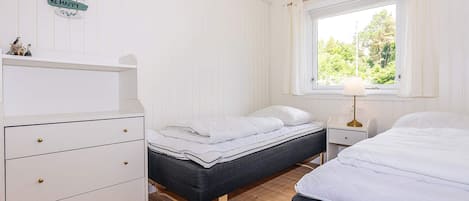 A room with two beds, a dresser, a window with curtains, and a wall-mounted sign.