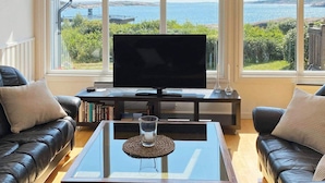 Een woonkamer met een grote televisie, leren banken en een glazen salontafel.