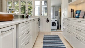 Een keuken met witte kastjes, een ingebouwde wasmachine en een blauw gestreept vloerkleed.