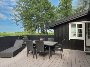 Un patio al aire libre con mesa y sillas, una terraza de madera y un edificio negro con una ventana.