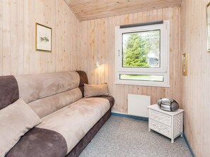 A cozy room with a sofa, a small white side table, and a window with a view of greenery.