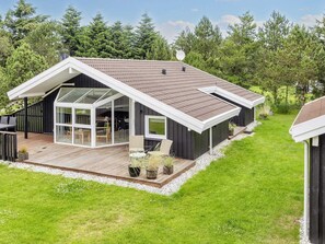 Ett modernt hus med en stor terrass, en inglasad uteplats och ett sluttande tak.