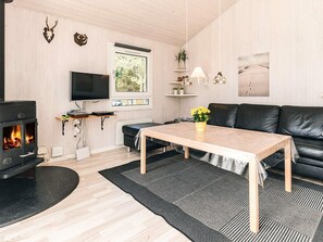 A modern living room with a fireplace, a black leather sofa, a wooden coffee table, and a TV mounted on the wall. - 4 Star Holiday Home in Lokken (Lokken)
