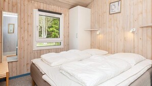 Une chambre avec deux lits, une fenêtre donnant sur les arbres, une table de chevet et un luminaire fixé au mur.