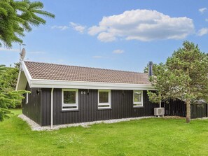A single-story house with a dark exterior, a tiled roof, and a small front yard with a tree and a fence.